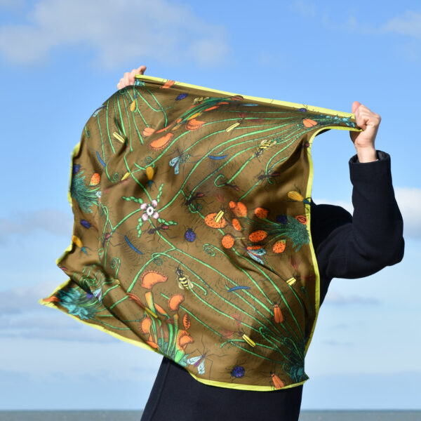 Homme caché par un grand foulard couleur café motif insectes et plantes carnivores qu'il tient devant lui, par grand vent