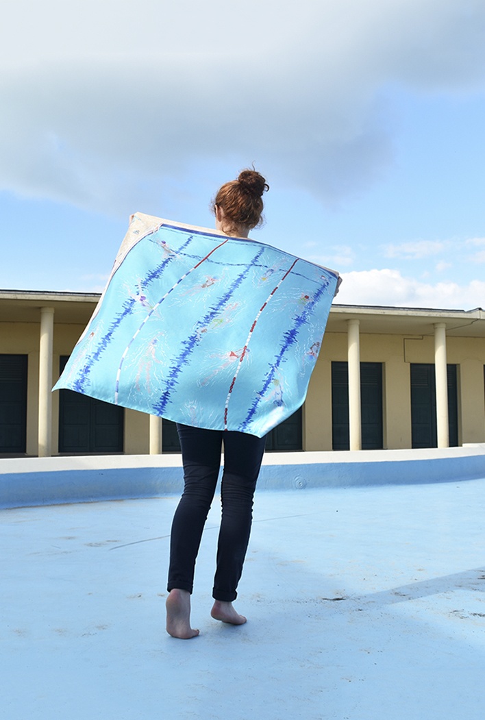 Jeune fille marchant de dos et tenant derrière elle un foulard comme une cape, représentant une piscine, dans un décor de piscine désaffectée (Deauville))