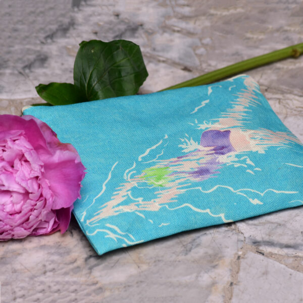 Pochette en tissu avec une fleur rose. Le motif sur la pochette représente une nageuse avec un maillot de bain violet sur fond bleu