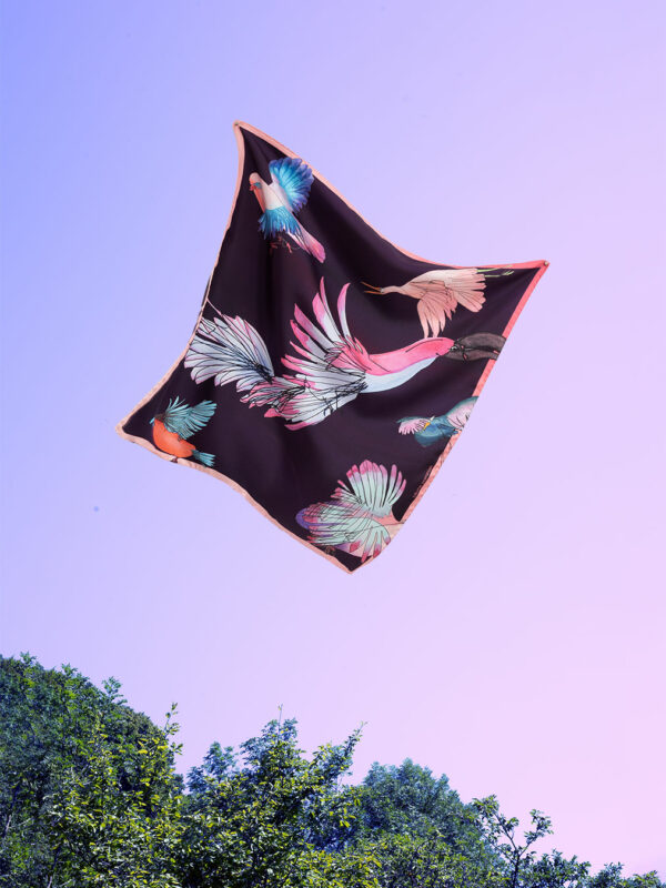 Foulard en soie au motif d'oiseau parme et rose sur fond violet foncé volant sur un ciel parme au dessus des arbres