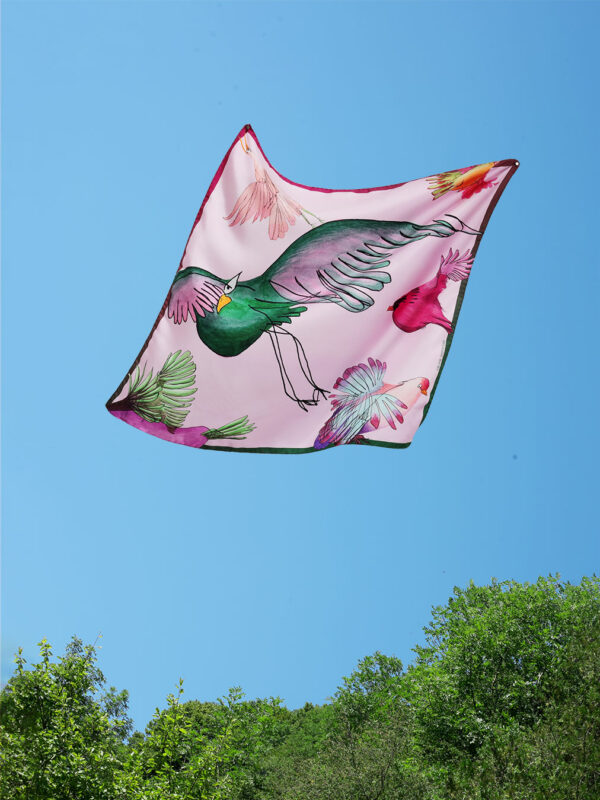 Foulard en soie au motif d'oiseau vert sur fond rose clair volant dans le ciel au dessus des arbres